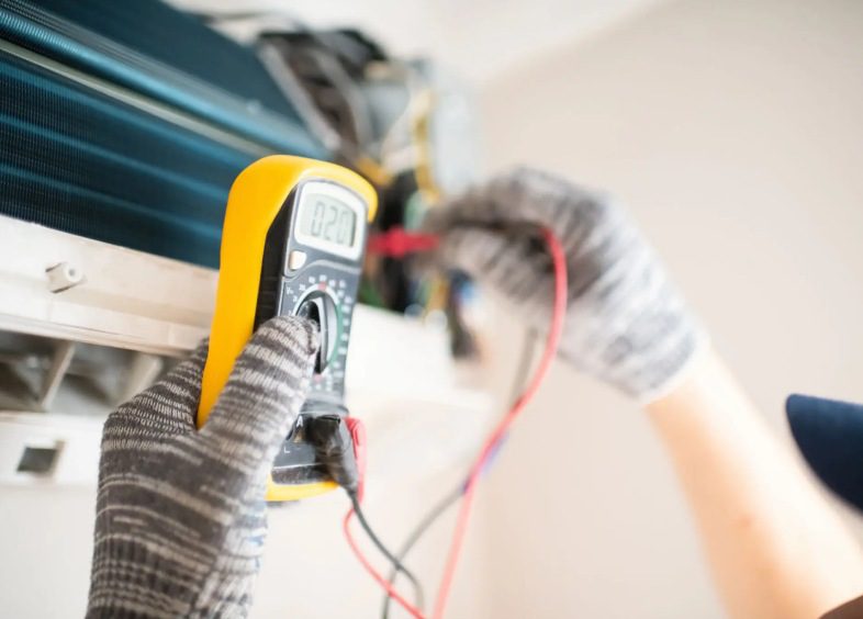 Technician using multimeter on air conditioning unit.
